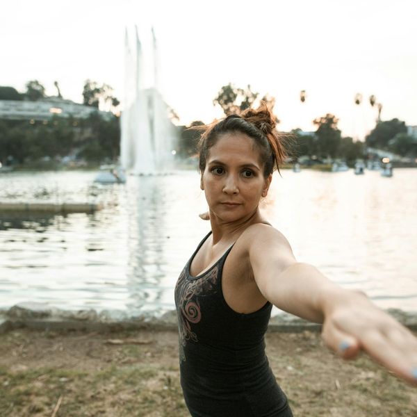 A pregnant woman doing a gentle and safe yoga stretch outdoors in a park.