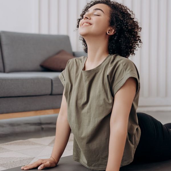 Smiling pregnant woman meditating peacefully on a yoga mat near a window.